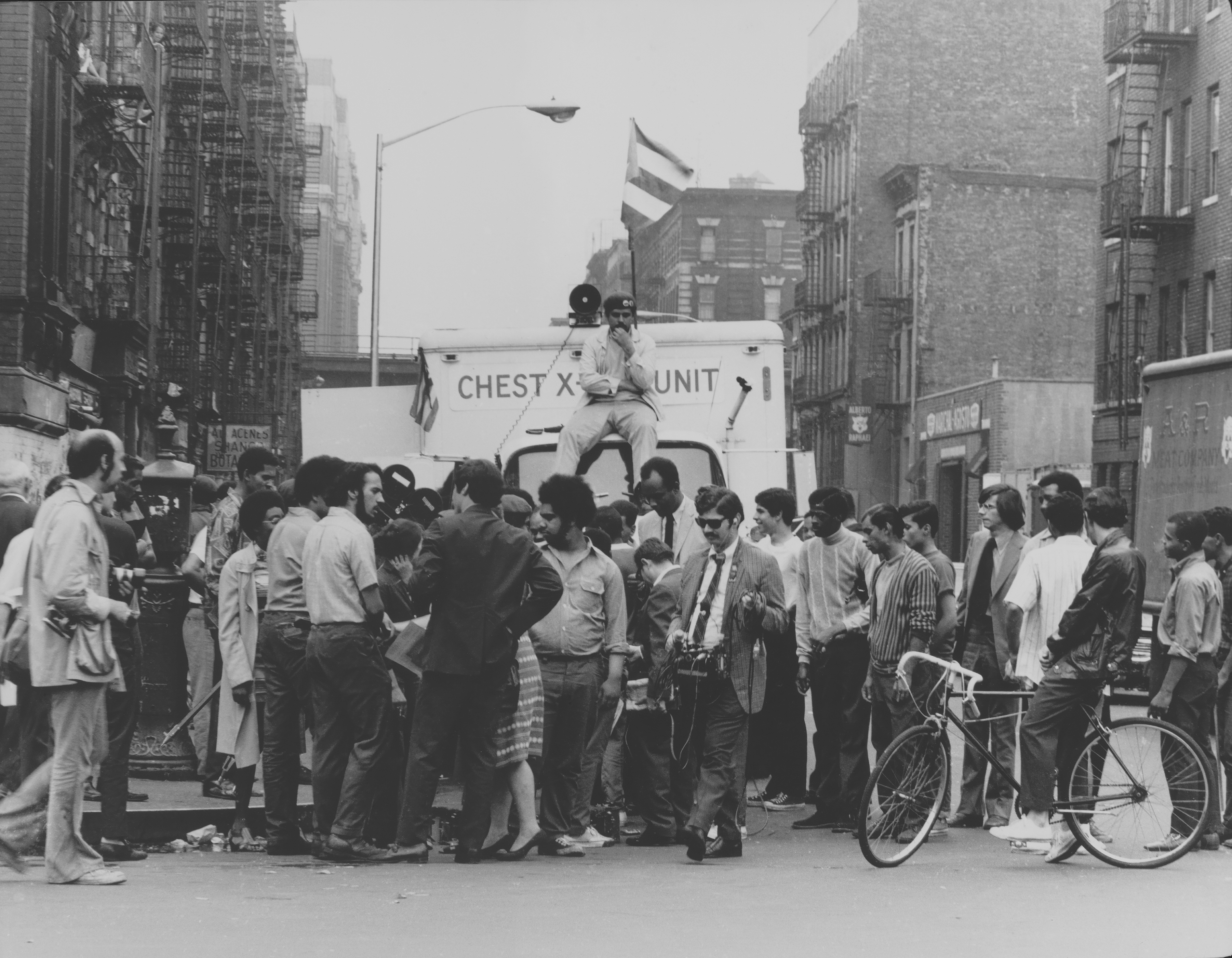 A crowd gathered in front of an X-ray unit truck. A man sits on the truck, staring at the camera.